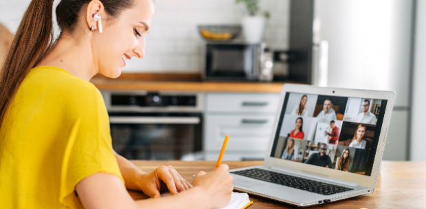 Woman in yellow blouse participating in online webinar and taking notes