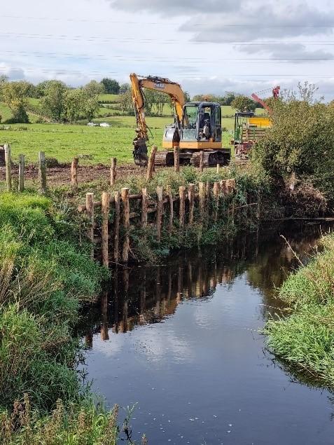 Digger doing work alongside a river bank with new fencing erected