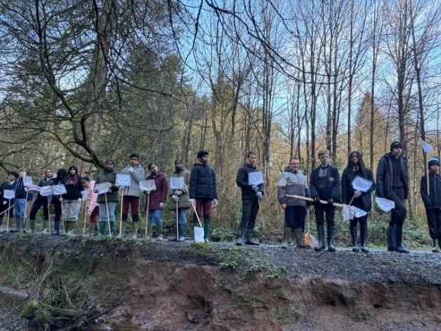 Group of post primary school children standing alongside a river bank with nets