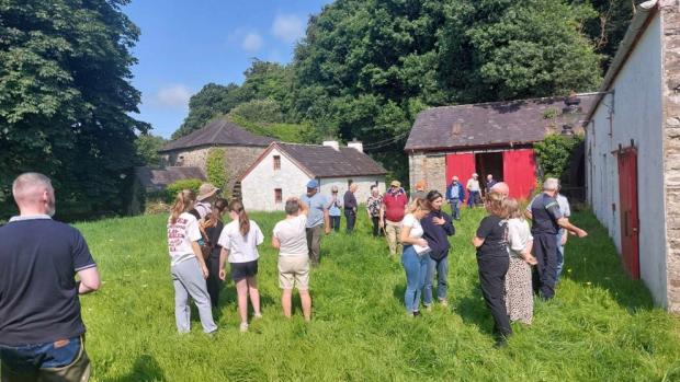 Group of people in a grassy field surrounded by outbuildings, attending community education workshop on acquatic invertebrates